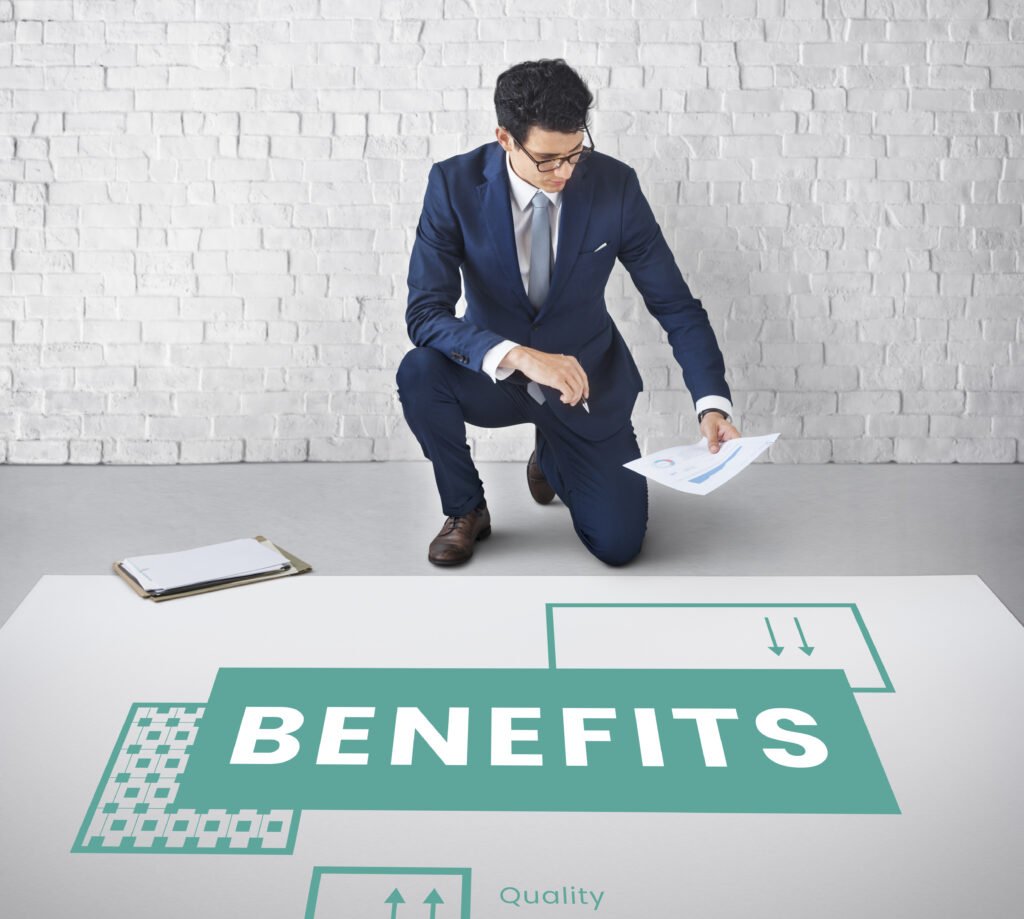 A business professional in a suit kneeling next to a large graphic displaying the word 'BENEFITS' along with various icons and diagrams representing quality and growth.