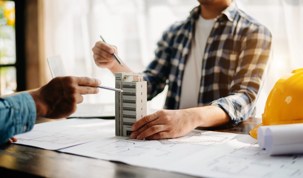 Two individuals discussing an architectural model of a building with blueprints spread out on the table.
The image represents collaboration in real estate development or construction planning.