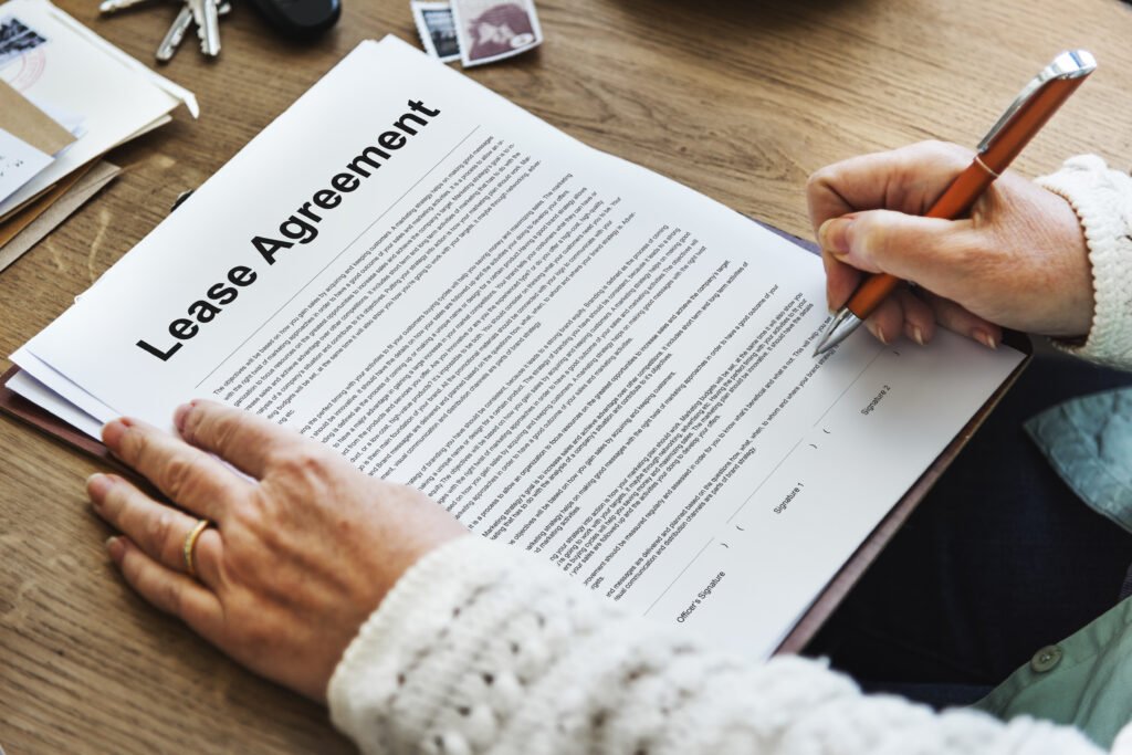 A close-up of a person's hands signing a lease agreement document with a pen, with visible legal text and signature lines.