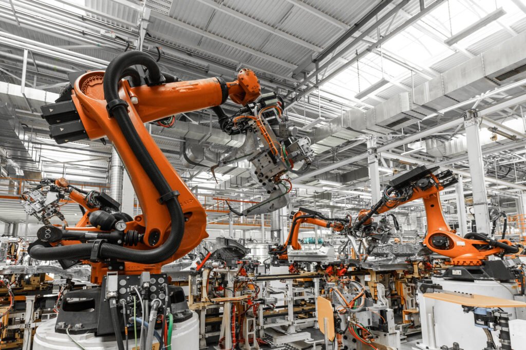 A row of orange robotic arms works on assembling machines in a modern industrial facility. The factory is equipped with advanced automation technology for precision manufacturing.